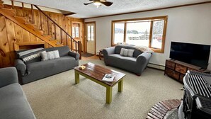 Ein Wohnzimmer mit Treppe, zwei Sofas, einem Couchtisch, einem Fernseher und einem Deckenventilator.