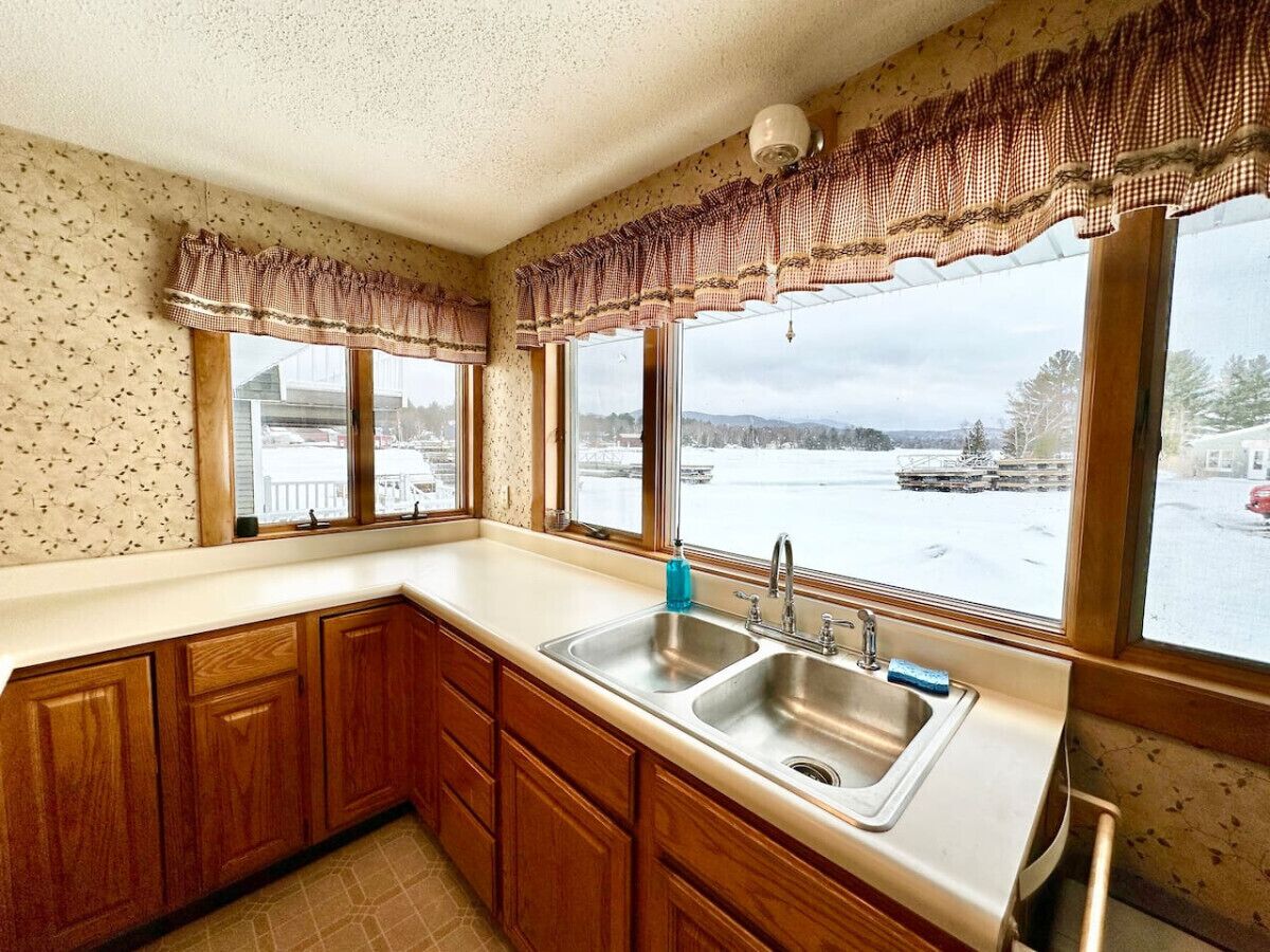 Eine Küche mit Holzausstattung, einer Spüle und Blick auf eine verschneite Landschaft durch große Fenster.