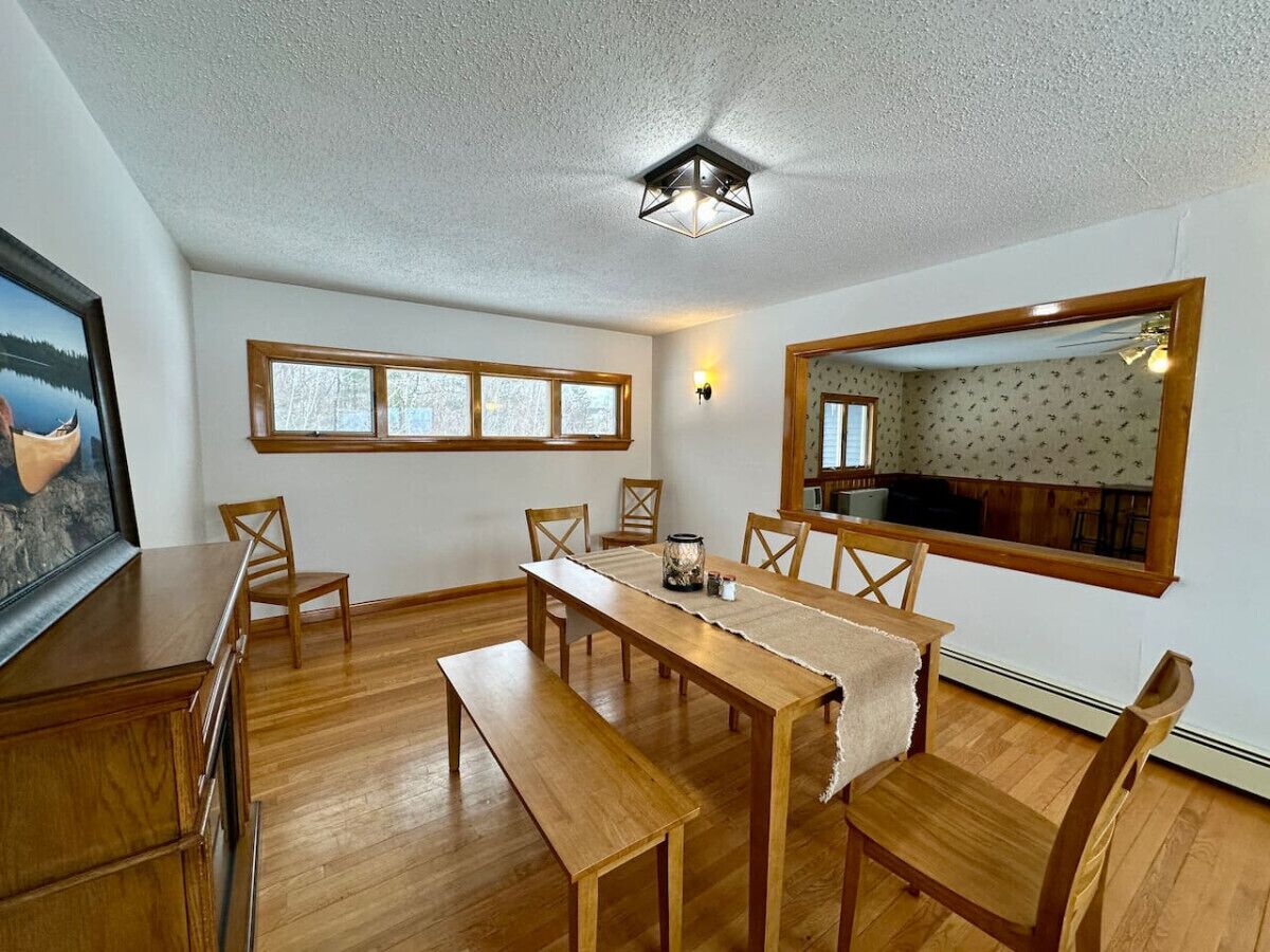 A dining area with a wooden table, benches, and chairs. There is a window with a view of trees and a framed picture on the wall.