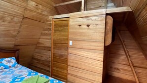 Ein gemütliches Schlafzimmer unter dem Dach mit schrägen Holzwänden, einem Bett mit gemustertem Überwurf und einer kleinen Holz-Laube.