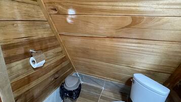 A wooden-paneled bathroom with a toilet, a small trash bin, and a toilet paper holder.