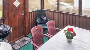 Un porche cubierto con una puerta de madera, dos sillas, una mesa y una planta en maceta.