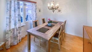 Un comedor con una mesa y sillas de madera, una araña y un ventanal con cortinas.