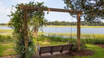A wooden swing set with a bench, surrounded by greenery and a lake view.