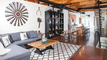 A modern living room with a gray sofa, wooden coffee table, and a patterned rug. A black bookshelf and a decorative fan are also visible.