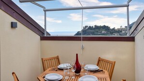 Een balkon met een eettafel, met uitzicht op een kustlandschap.