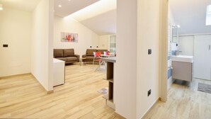 Een modern appartement met een zithoek met een bank en stoelen, een eettafel met stoelen, en een keuken met een spoelbak en aanrecht.