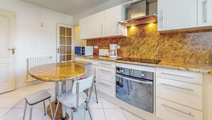 Una cocina compacta con armarios blancos, encimera de granito, horno integrado y cafetera.