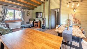 Un acogedor interior de cabaña con una mesa de comedor de madera, un sofá, una chimenea y un ventanal con cortinas.
