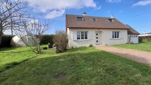 Une maison de plain-pied avec un toit en tuiles, des murs extérieurs blancs et un petit jardin devant, avec un chemin de gravier.