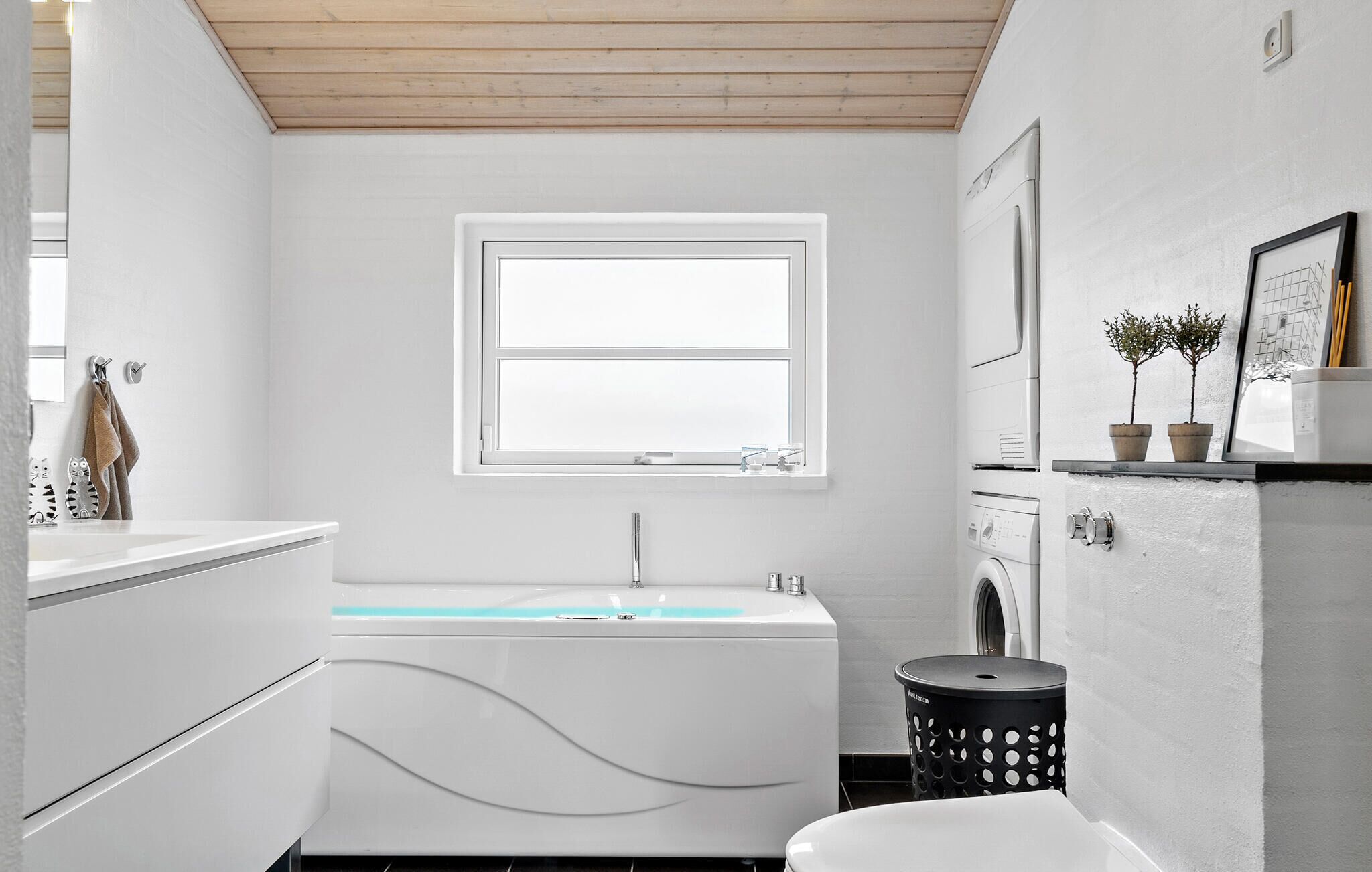 Ein modernes Badezimmer mit Badewanne, einem Fenster, einer Waschmaschine und einer kleinen Ablage mit Pflanzen.