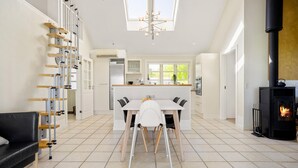 A modern kitchen with a central island, a dining area with a white table and chairs, a black sofa, and a fireplace. - Lovely home in Orø with house sea view (Orø)