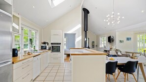 A modern kitchen with white cabinetry, a central island, and a large window. - Lovely home in Orø with house sea view (Orø)