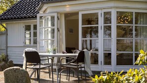 A cozy outdoor seating area with a table and chairs, a potted plant, and a view through large windows. - Lovely home in Orø with house sea view (Orø)