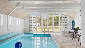 Ein überdachter Pool mit großen Glasfenstern, Fliesenboden und einer Decke mit geometrischem Muster.