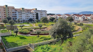 A residential area with multi-story apartment buildings, a well-maintained garden with various plants and trees, and a clear view of distant mountains. - Park Snail - Alghero Loc. Caragol   (Alghero)