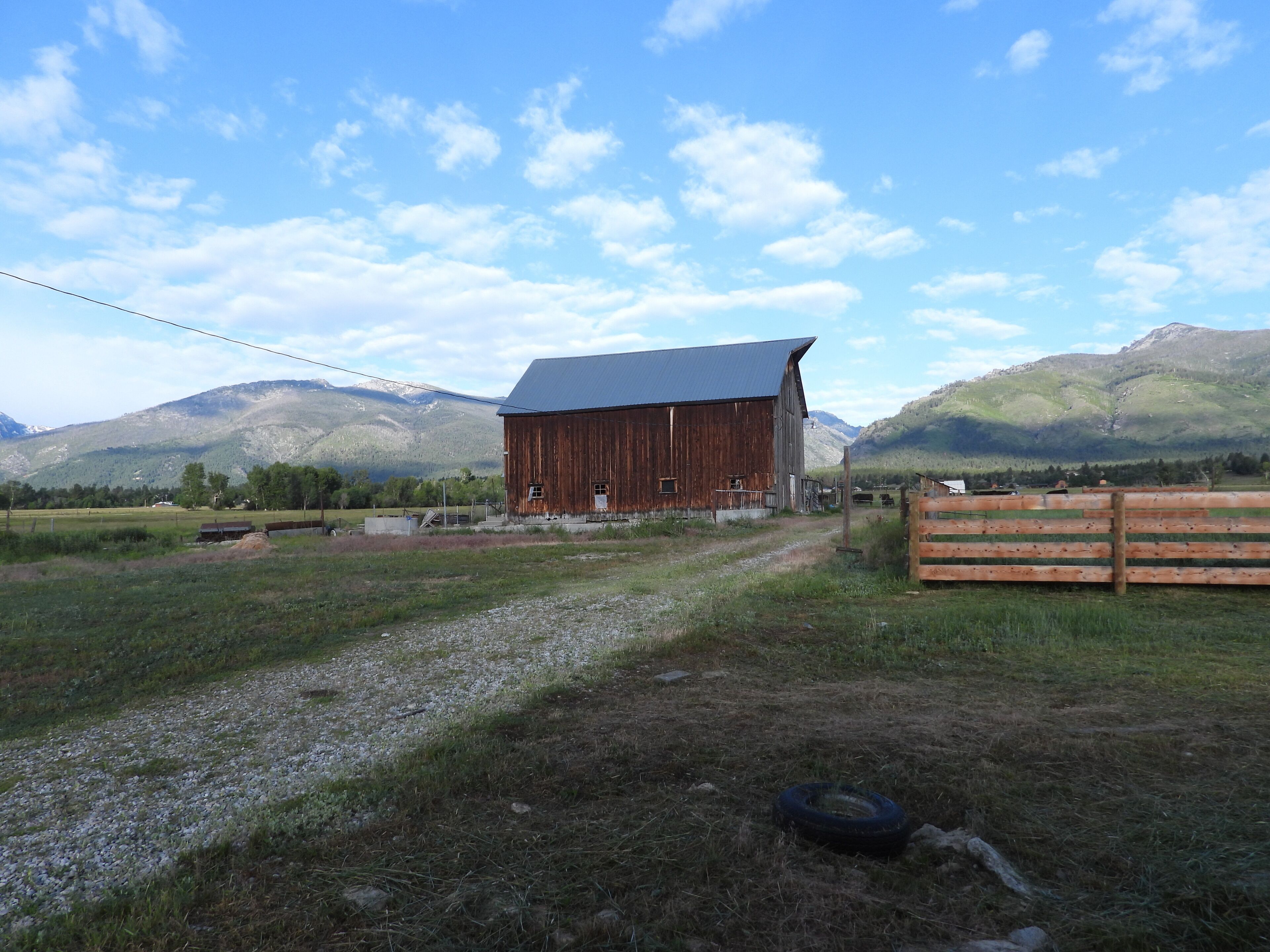 A rustic barn with a metal roof, surrounded by a gravel path and a wooden fence.