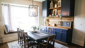 Un espace repas comprenant une table, des chaises et un coin cuisine avec des placards bleus et des étagères en bois.