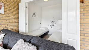 Une pièce chaleureuse avec un canapé gris, un lit blanc et une petite table blanche. Les murs sont décorés, notamment avec des motifs de hiboux et d’arbres.