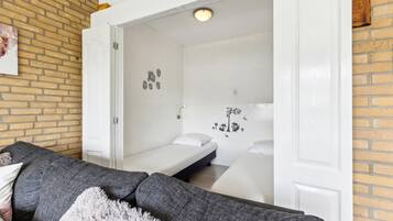Ein gemütliches Zimmer mit einem grauen Sofa, einem weißen Bett und einem kleinen weißen Tisch. An den Wänden sind Dekorationen zu sehen, darunter Eulen und ein Baum.