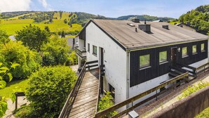 Un bâtiment moderne doté d’un toit plat, d’un balcon et offrant une vue sur des champs verdoyants et des collines.
