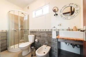 A bathroom with a glass-enclosed shower, a toilet, a bidet, a sink with a mirror, and a window above the sink. - Art Hotel FyF (Punta del Este)
