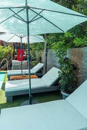 A poolside area with lounge chairs, a large umbrella, and a small pool. - Art Hotel FyF (Punta del Este)