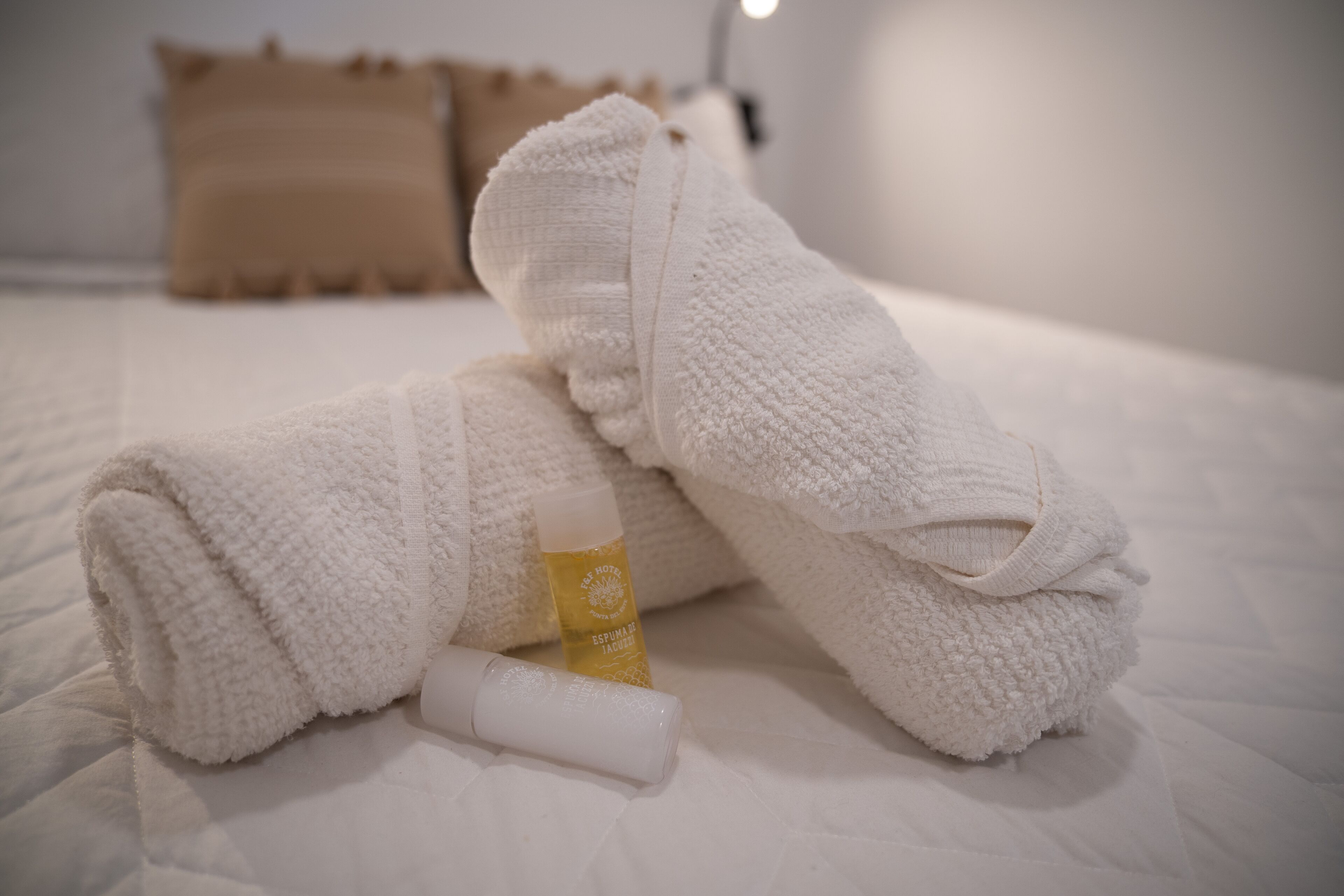 A neatly made bed with white towels and a bottle of lotion.