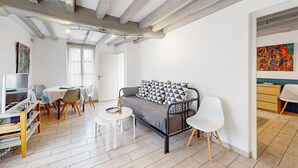 Een moderne woonkamer met een bank, een eettafel en stoelen. Er staat een tv op een dressoir, een boekenkast en een schilderij hangt aan de muur.
