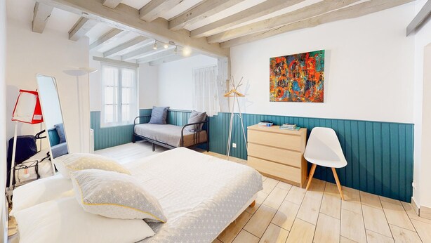 Een slaapkamer met een bed, een dressoir, een stoel en een schilderij aan de muur.