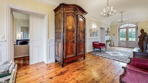 Una habitación amplia con suelo de madera, un mueble de madera grande, un sillón rojo y una estatua.