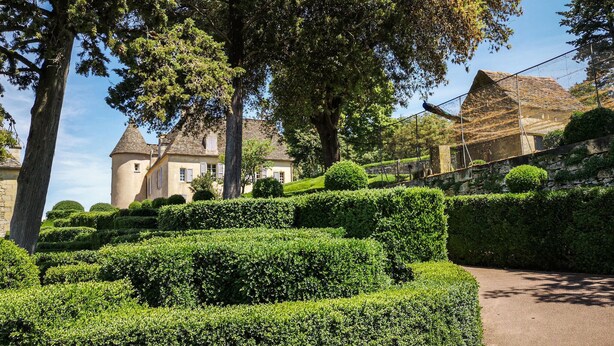 Un jardín bien cuidado con setos ordenados y un edificio tradicional con una torre.