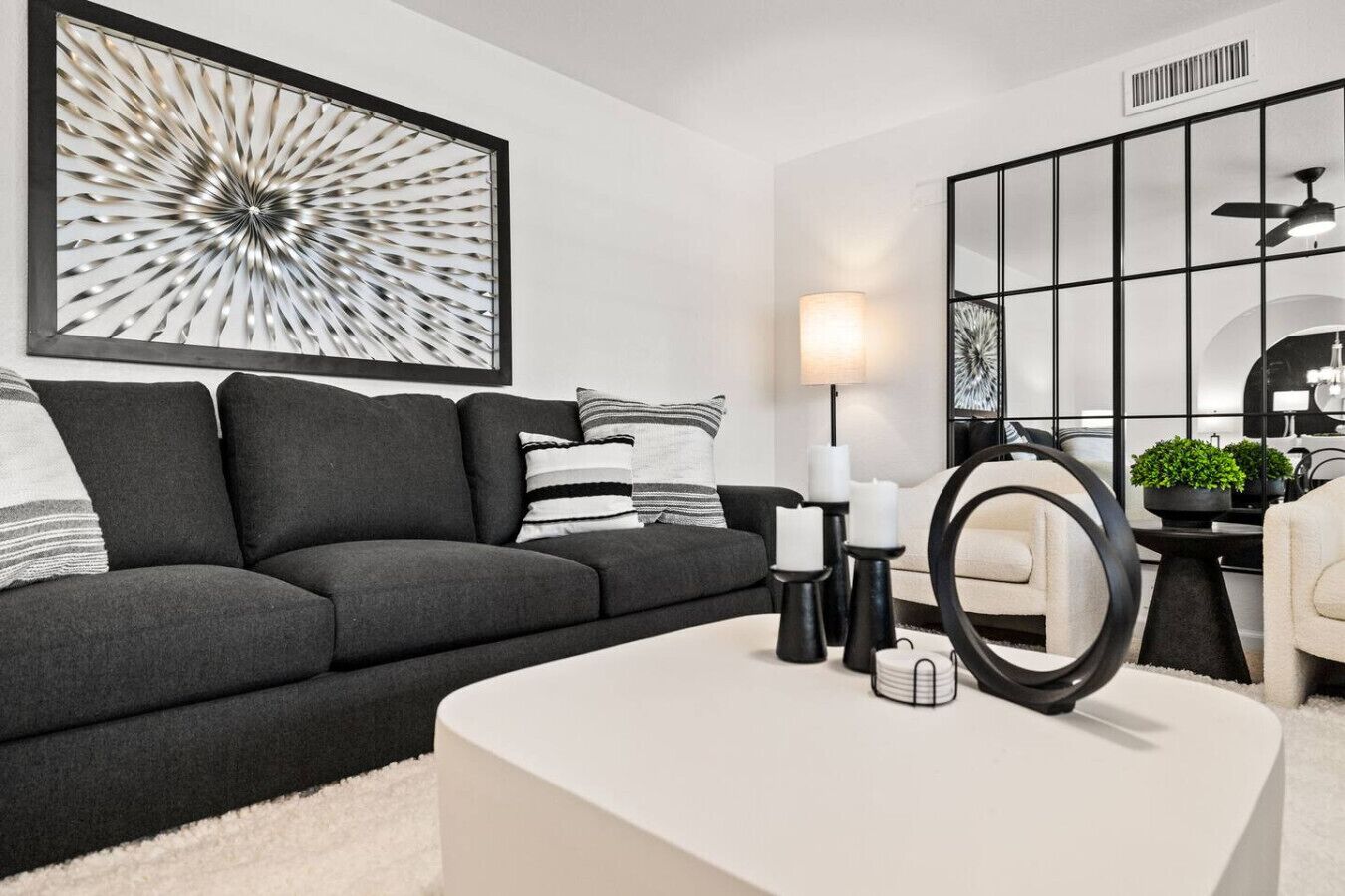 A modern living room with a dark grey sofa, white cushions, a white coffee table, and a large abstract painting on the wall.
