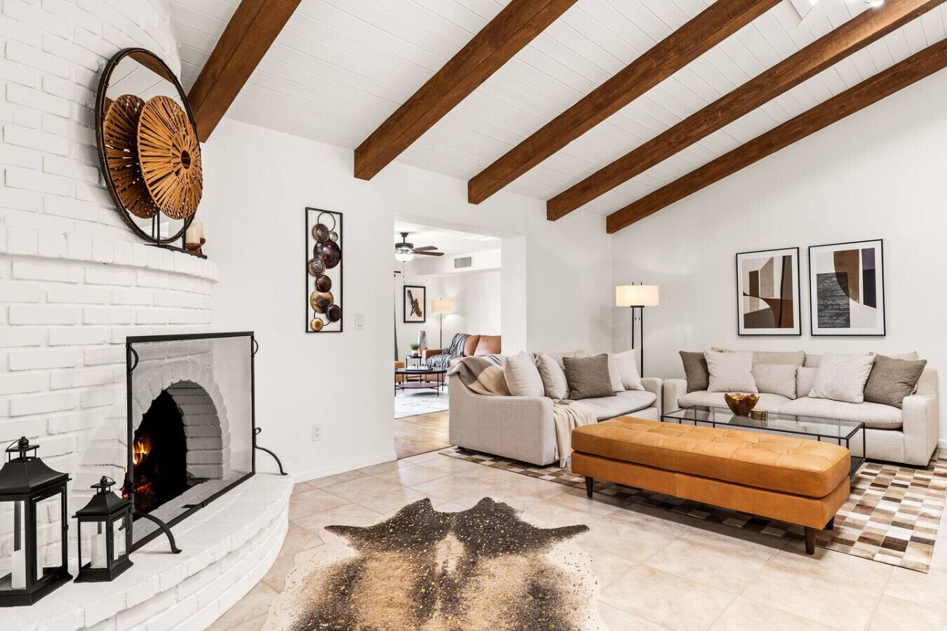A modern living room with a fireplace, white brick walls, wooden beams, and a checkered rug.