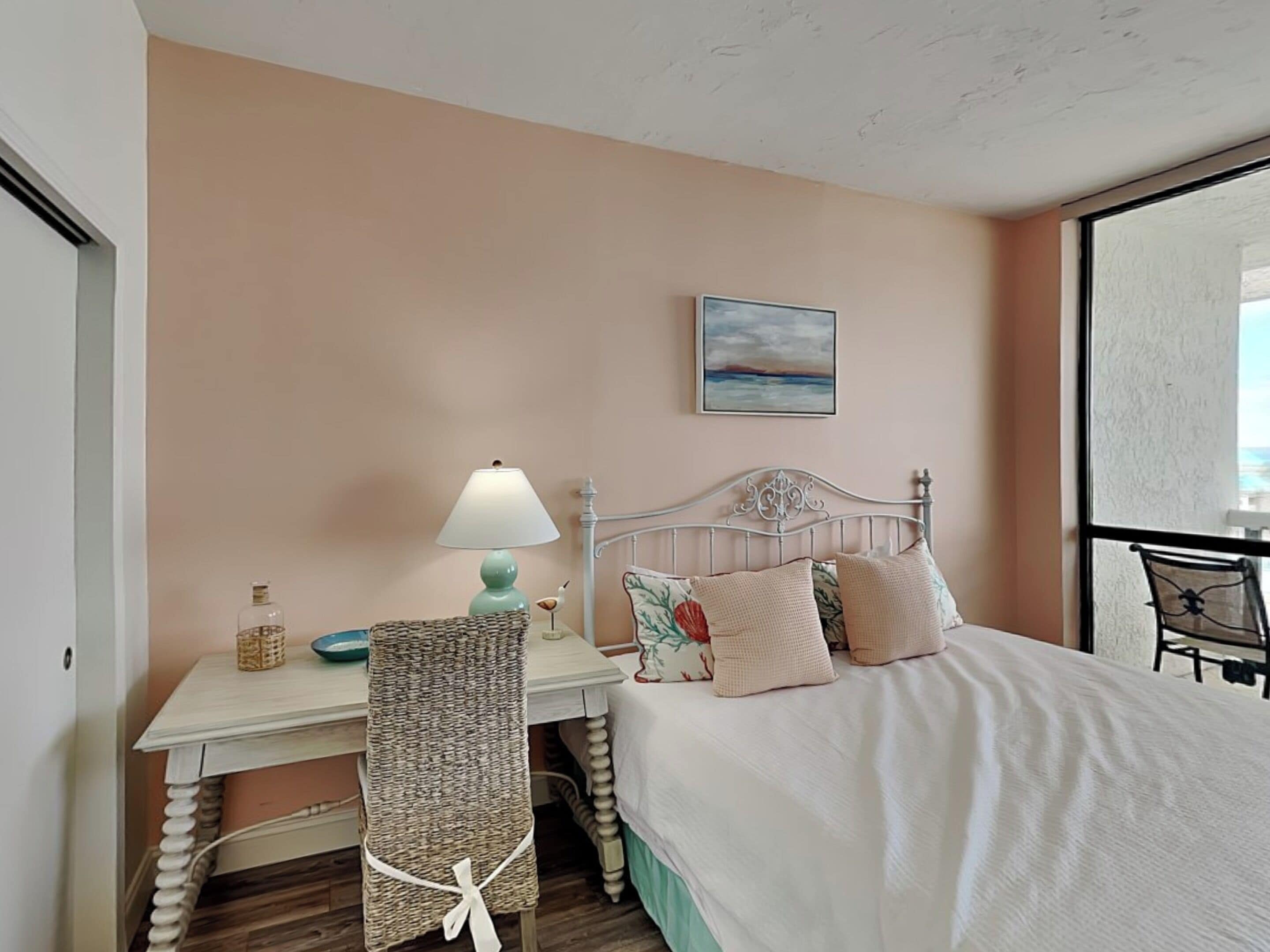 A bedroom with a bed, a bedside table with a lamp, a chair, and a window with a view.