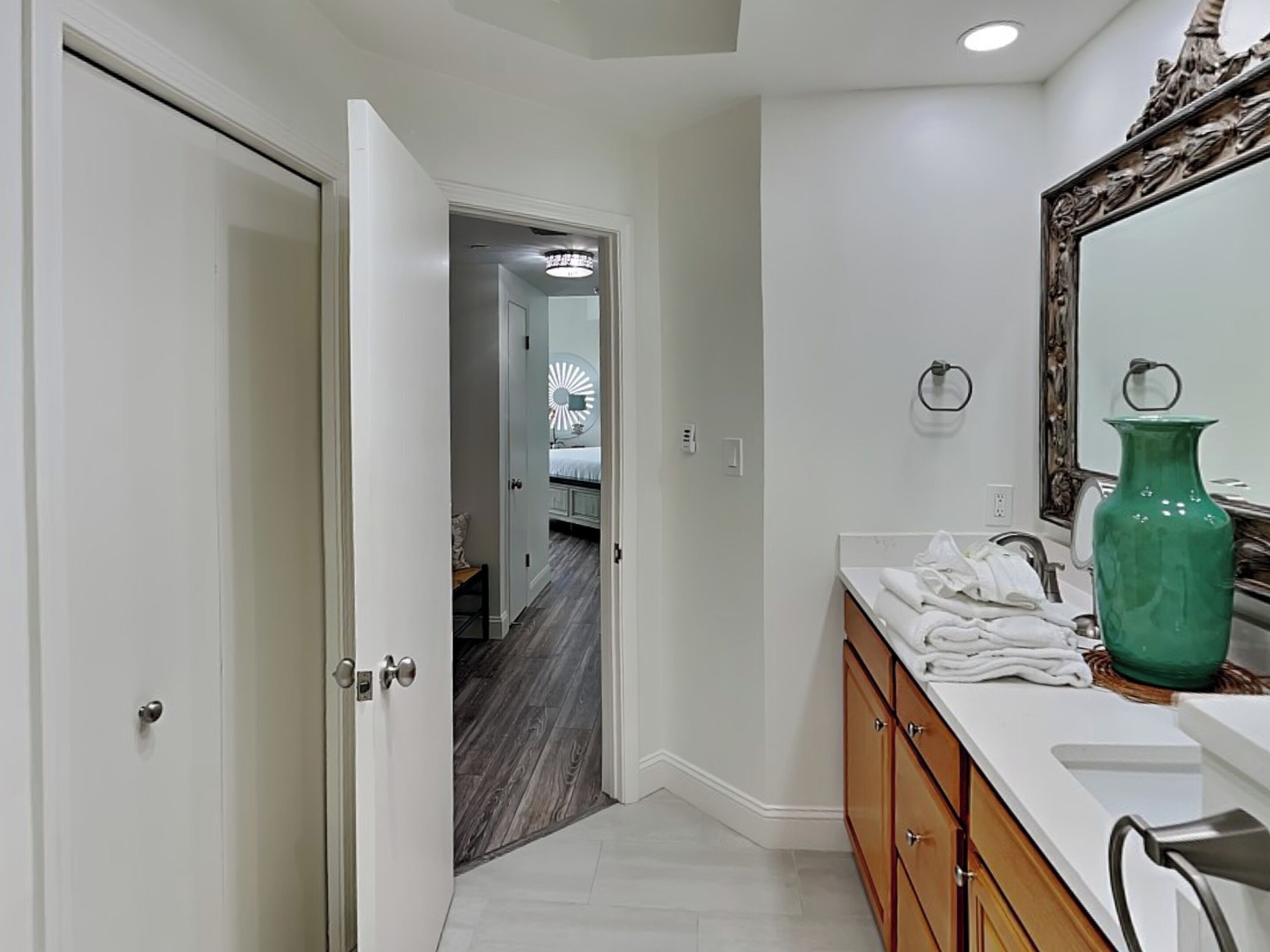 Un baño con tocador blanco, un jarrón verde y un espejo con marco decorativo.