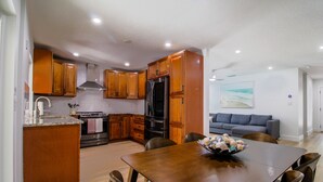 A modern kitchen with wooden cabinets, a dining table, and a gray couch in the adjacent living area. - Sarasota modern house, heated saltwater pool, close to beaches and downtown! (Sarasota)
