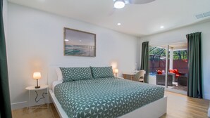 A bedroom with a large bed, a small bedside table with a lamp, a chair, and a view of an outdoor area with a table and chairs. - Sarasota modern house, heated saltwater pool, close to beaches and downtown! (Sarasota)