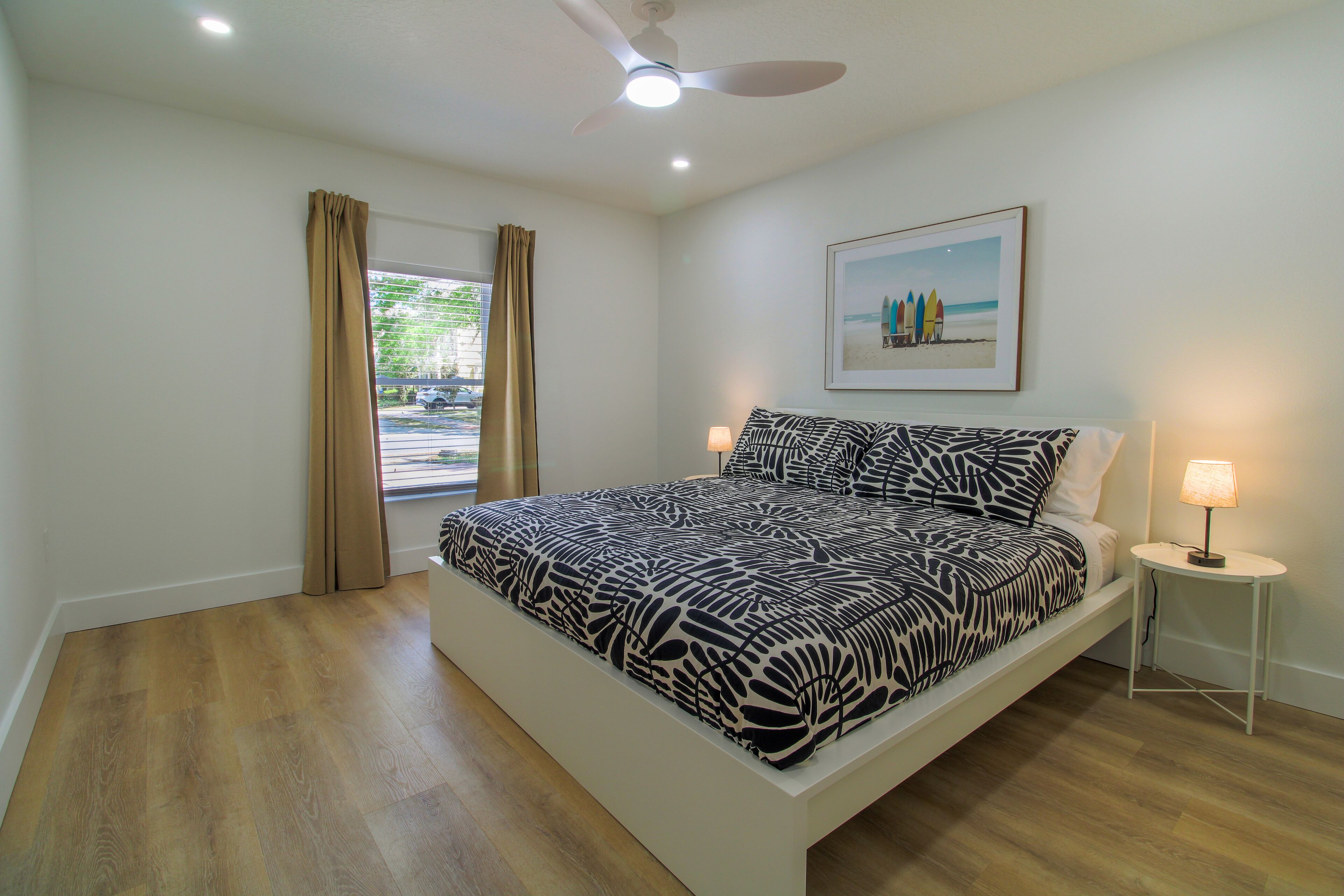 A bedroom with a bed, a ceiling fan, a window with curtains, and a wall-mounted picture.