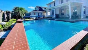 A swimming pool with a wooden deck, a covered patio area, and a house in the background. - 5minutes direct to Kemah with the beaches and countless seafood restaurants  (Seabrook)