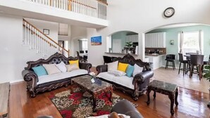 A spacious living room with a high ceiling, a staircase, and a kitchen in the background. - 5minutes direct to Kemah with the beaches and countless seafood restaurants  (Seabrook)