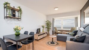 A modern living room with a dining area, a sofa, a TV, and a view of the sea. - Cozy apartment in Oostende with WiFi (Oostende)