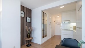 A modern kitchen with white cabinets, a black chair, and a vase with dried flowers on a small table. - Cozy apartment in Oostende with WiFi (Oostende)
