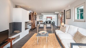 A modern living room with a fireplace, a sofa, a coffee table, and a dining area in the background.