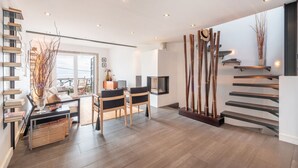 A modern living room with a staircase, a dining area, and a bookshelf.