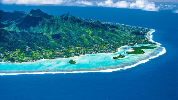 An aerial view of a tropical island with mountainous terrain, a coastline, and clear turquoise waters. - Mangavai Bungalow (Rarotonga)