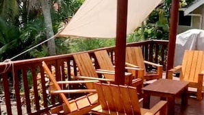 A wooden deck with outdoor furniture, including chairs and a table, under a shaded area with a canopy. - Mangavai Bungalow (Rarotonga)