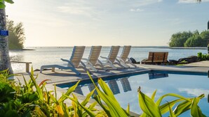 A poolside area with lounge chairs and a wooden bench, overlooking a body of water. - Mangavai Bungalow (Rarotonga)
