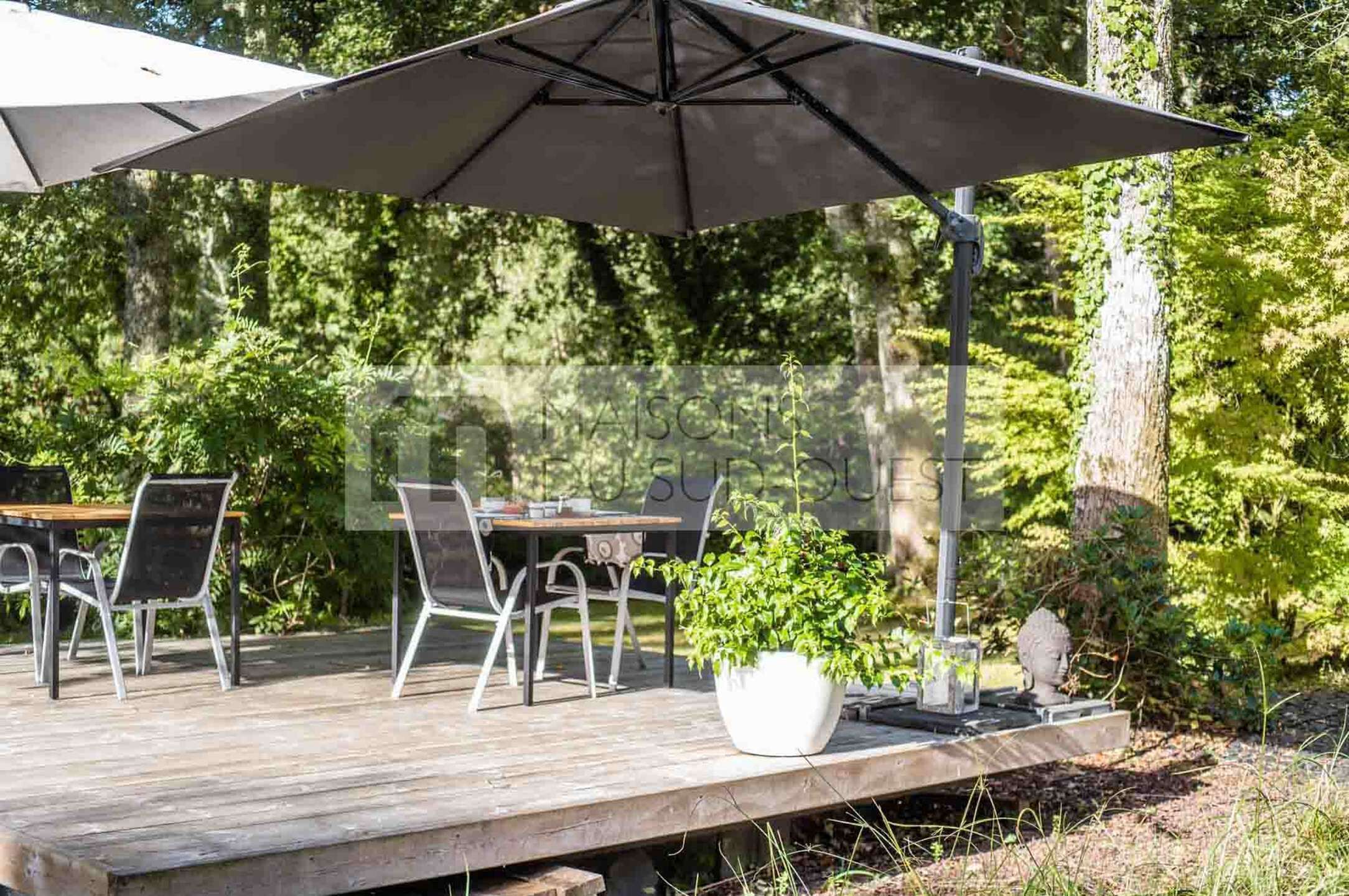 A wooden deck with outdoor furniture, a large umbrella, and a potted plant.