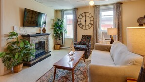 Un salon avec une cheminée, un canapé, une table basse, un téléviseur et une horloge au mur.